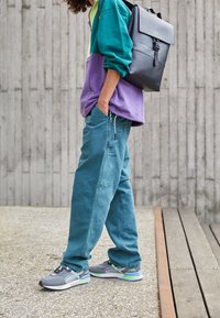 Colorful oversized hoodie in teal and purple, relaxed-fit teal pants, and gray-green sneakers with blue accents; black backpack with flap.