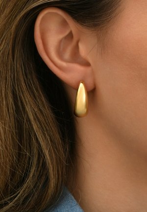 Boucle d'oreille en forme de goutte d'eau en or avec une surface lisse et réfléchissante, portée par un mannequin près de l'oreille, présentant un design simple et élégant.