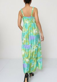 Robe maxi en tissu doux, avec un corsage froncé et une jupe à plusieurs niveaux. Les couleurs incluent le vert, le bleu et la lavande avec un motif subtil.