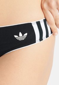 Svart bikini underdel med vita detaljer och en design med tre ränder. Inkluderar en vit Adidas-logotyp på vänster sida. Mjuk tygkvalitet.