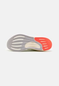 Sole of athletic shoe featuring a grey and red rubber pattern, textured grooves, and a soft cream midsole for cushioning.
