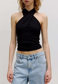 Zwarte haltertop met een gedraaide voorkant, gemaakt van rekbare stof, gecombineerd met lichtblauwe hoge taille spijkerbroek met zakken.