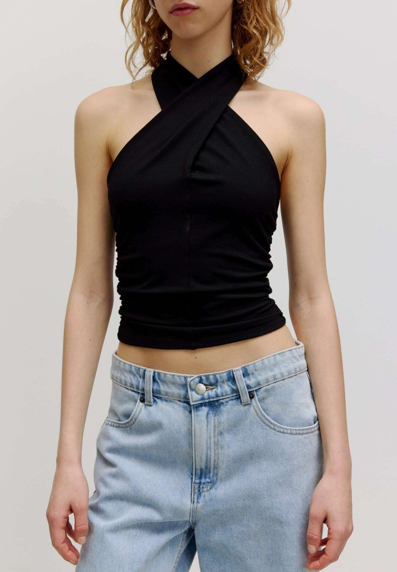 Zwarte haltertop met een gedraaide voorkant, gemaakt van rekbare stof, gecombineerd met lichtblauwe hoge taille spijkerbroek met zakken.