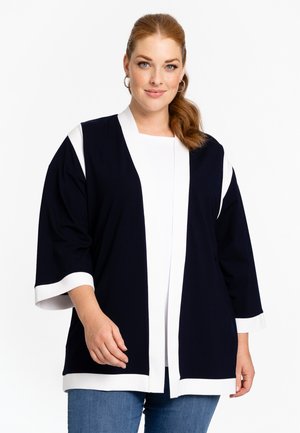 Navy blue kimono-style jacket with white accents, broad sleeves, open front, and soft, smooth texture, paired with a white top and blue jeans.