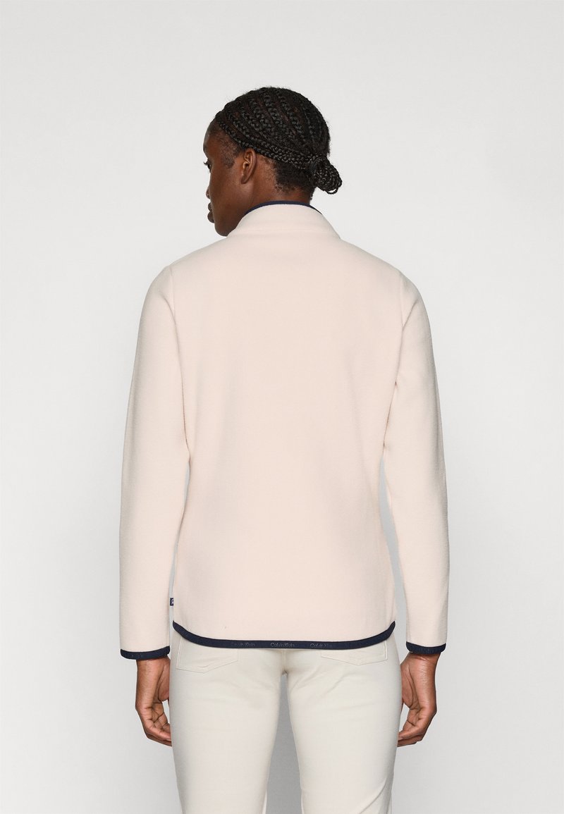 Helles rosa Fleece-Jacke mit hohem Kragen, langen Ärmeln und marineblauen Abschlüssen an den Bündchen und dem Saum. Glatte Textur, keine sichtbaren Muster.
