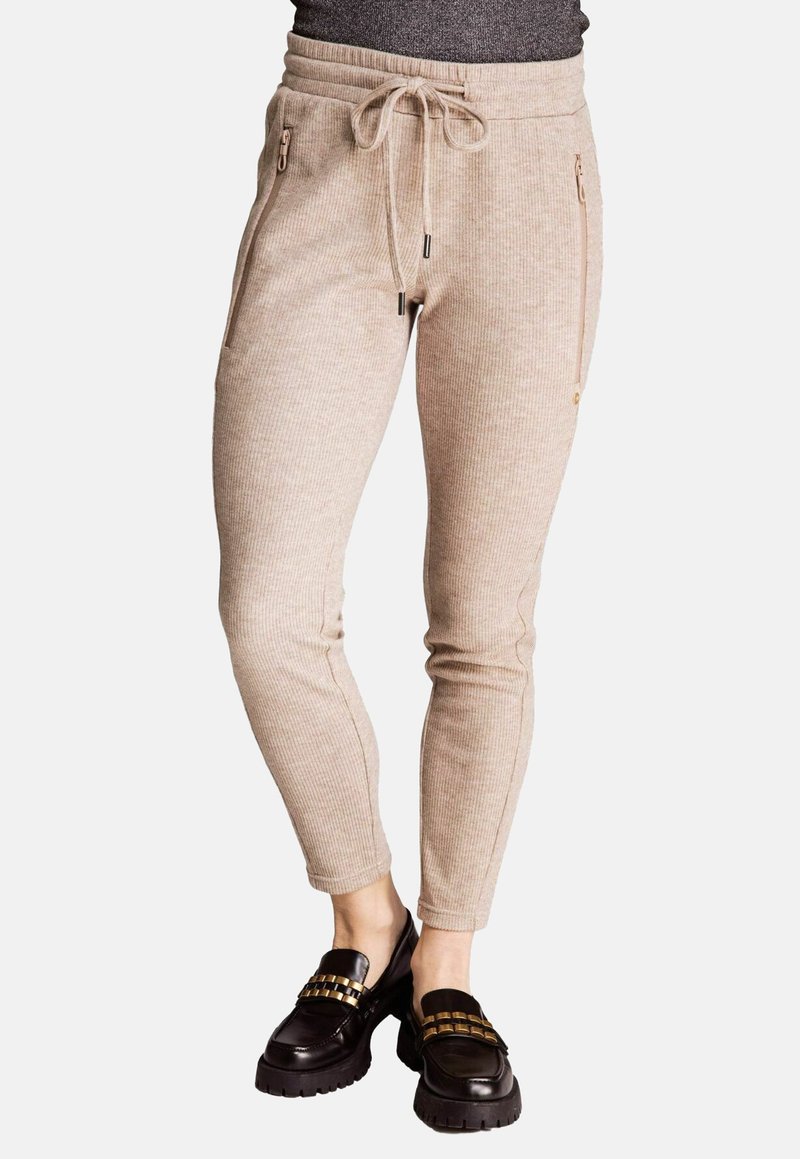 Beige, gerippte Jogginghosen mit einem Kordelzugbund, seitlichen Reißverschlusstaschen und einem schmal zulaufenden Bein, kombiniert mit klobigen schwarzen Loafers.