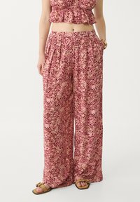 Vrouw in roze gestreepte wijde broek met zijzakken en bijpassende cropped top, gecombineerd met tan gespsandalen.