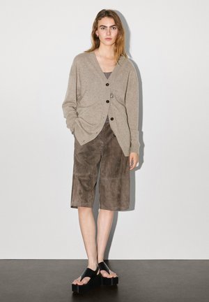 Beige wool blend cardigan with large black buttons, paired with brown suede shorts. Black platform sandals complete the outfit.