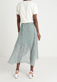 Florale midi-rok in lichtgroen met delicate zwarte accenten, vloeiende stof en een high-low zoom, gecombineerd met een eenvoudig wit t-shirt en schoenen.
