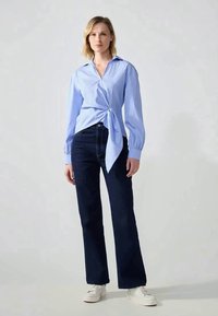 Lichtblauw en witte gestreepte shirt met een knoop aan de voorkant, gecombineerd met donkerblauwe flared jeans en witte sneakers. Soepele textuur en slim-fit ontwerp.