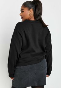Svart oversized sweatshirt med rund hals och sänkta axlar, kombinerad med en mörk denim minikjol med synliga fickor och fransad fåll.