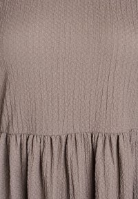 Volné šaty v světle taupe barvě, vyrobené z texturované, mačkané látky. Design zahrnuje nashromážděný, nařasený lem v oblasti pasu.