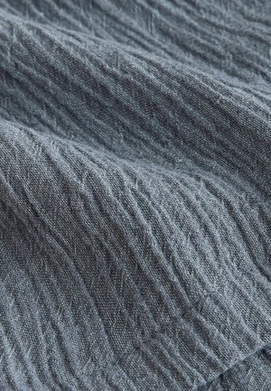 Pelēks audums ar tekstūru un mīkstu, saburzītu izskatu. Redzams viegls pinums ar dažādām virsmas struktūrām, kas liecina par dabiska un organiska rakstura sajūtu.