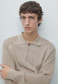 Maglione tipo polo beige lavorato a maglia con colletto, tre bottoni e dettagli a coste su spalle e polsini. Texture morbida, vestibilità comoda.