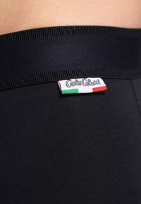 Zwarte stof met een brede, gestructureerde tailleband met een gestikt logo-label in wit, rood en groen. Glad, rekbaar materiaal.