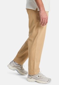 Beige katoenen broeken met rechte pijpen, voorzien van zijzakken. Gepaard met lichtgrijze mesh sneakers met witte accenten en veters.