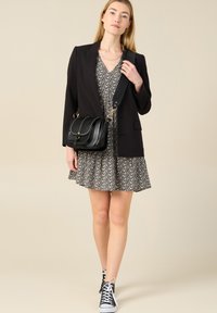 Blazer negro ajustado sobre un vestido con estampado floral. Bolsa cruzada negra con detalles de tachuelas. Zapatillas altas en blanco y negro.