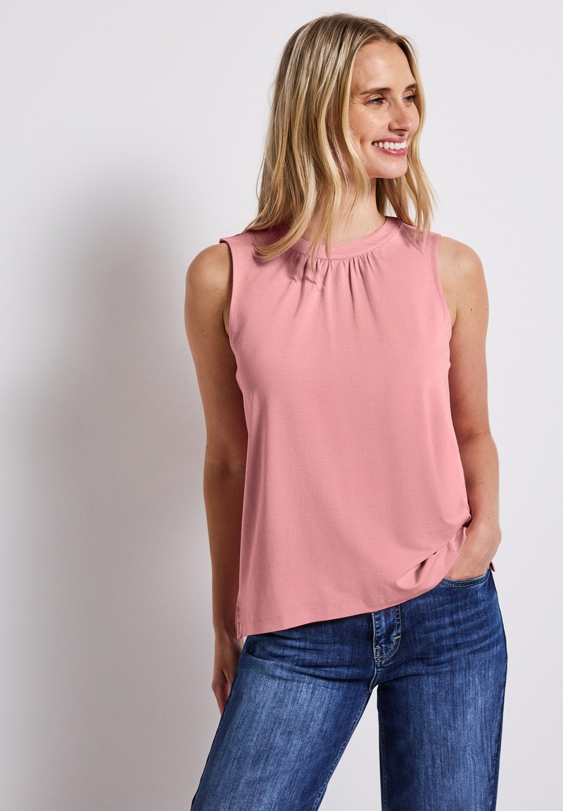 Haut sans manches rose avec un décolleté froncé, en tissu doux, coupe décontractée, associé à un jean en denim bleu. Design simple sans motifs.