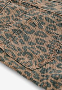 Leopardenmusterstoff mit beigem Hintergrund und dunkelgrünen Punkten, strukturierte Oberfläche und sichtbare Nähte an den Taschenrändern.