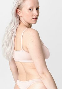Lichtroze lingerieset van een gladde, elastische stof. De beha heeft dunne, verstelbare bandjes en een eenvoudige sluiting op de rug; bijpassende bikini-achterkant.