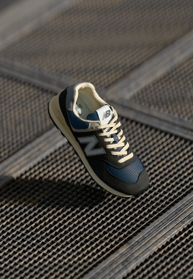 Zapatillas negras y marinas con un cuerpo de malla, acentos de ante y cordones crema. Presenta un destacado logo 'N' gris en el lateral. Punta redondeada.