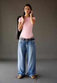 Světle růžový body, oversized modré džíny, hnědý pásek, měkké světlé boty, stylizované s tmavým sakem přehozeným přes jedno rameno.