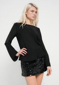 Haut noir à manches longues avec poignets évasés associé à une jupe courte noire en sequins. Tissu doux, texture lisse et finition brillante en sequins.