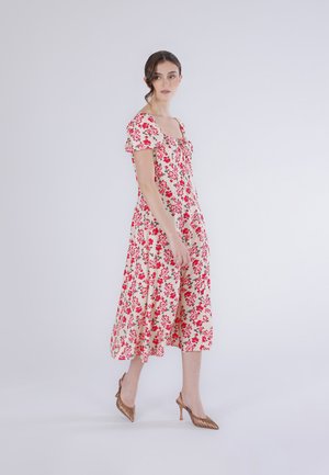 Kvinde går iført en hvid midi-kjole med rødt blomstermønster og puffede ærmer, kombineret med bronzefarvede spidse højhælede sko.