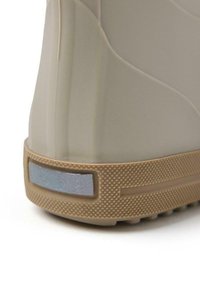 Sneaker beige con suola in gomma testurizzata e accentuazione riflettente. Presenta un design morbido e arrotondato con linee di contorno sottili sulla parte superiore.
