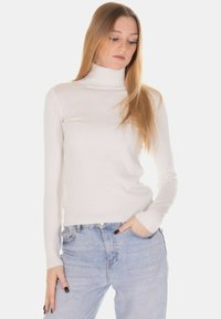 Maglione bianco a collo alto con texture a coste, design aderente, maniche lunghe, abbinato a jeans a vita alta azzurri chiari.