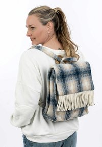 Faux-Fur-Rucksack mit blau-beigem Karomuster, fransigen Details am Boden und Stoffträgern. Weiche Textur und strukturierte Form.