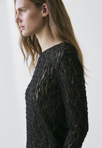 Black lace knit top with a textured pattern, long sleeves, and a boat neckline. Sheer fabric shows skin underneath.