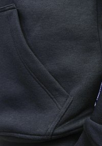 Svart sweatshirttyg med en texturerad yta, som har en framficka och synliga sömnadsdetaljer. Slät och mjuk känsla överlag.