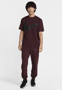 Burgundy Nike t-shirt med svart logotyp, tillsammans med matchande joggers med en subtilt märke tryck. Avslutat med svarta träningsskor.