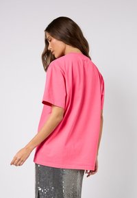 Růžové bavlněné tričko s volným střihem, krátkými rukávy a kulatým výstřihem. Bez viditelných vzorů nebo kovových doplňků. Hladká textura.
