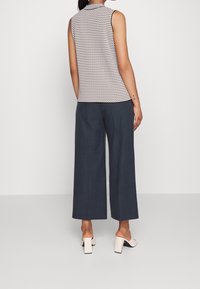 Top bez rękawów z geometrycznym wzorem w białym i granatowym kolorze, zestawiony z szerokimi granatowymi spodniami. Obuwie ma blokowy obcas w kolorze ecru.