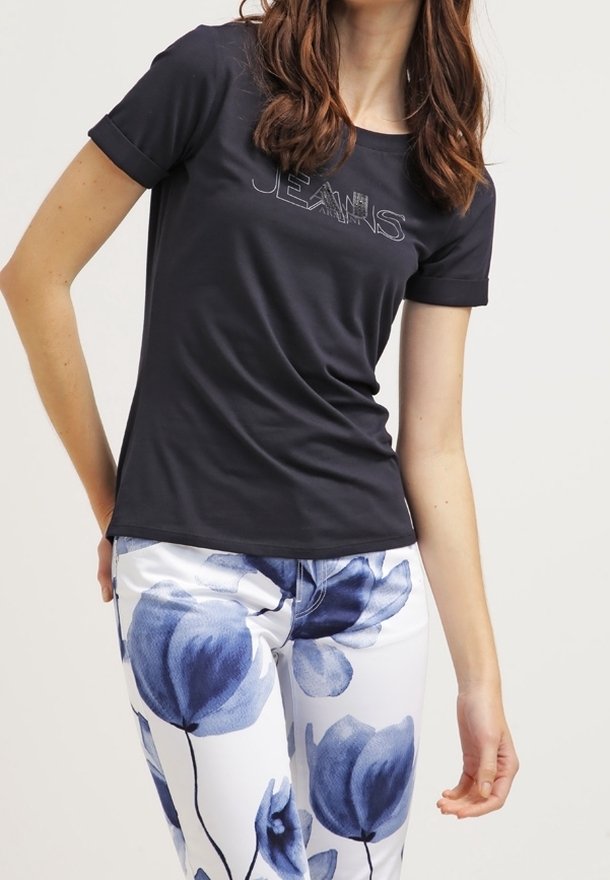 Černé tričko s krátkým rukávem se strukturálním nápisem "JEANS", v kombinaci s bílými kalhotami s modrými květinovými vzory.