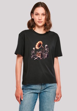 Schwarzes Baumwoll-T-Shirt mit einem zentralen Grafikmotiv von zwei Skelette um ein vintage Grammophon, mit verstreuten Schallplatten auf dem Boden.
