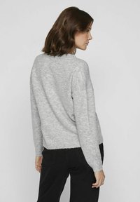 Hele halli kudumüts pika varrukaga ja ümmarguse kaelusega, millel on vaba lõige ja tekstureeritud viimistlus. Kombineeritud mustade pükstega.