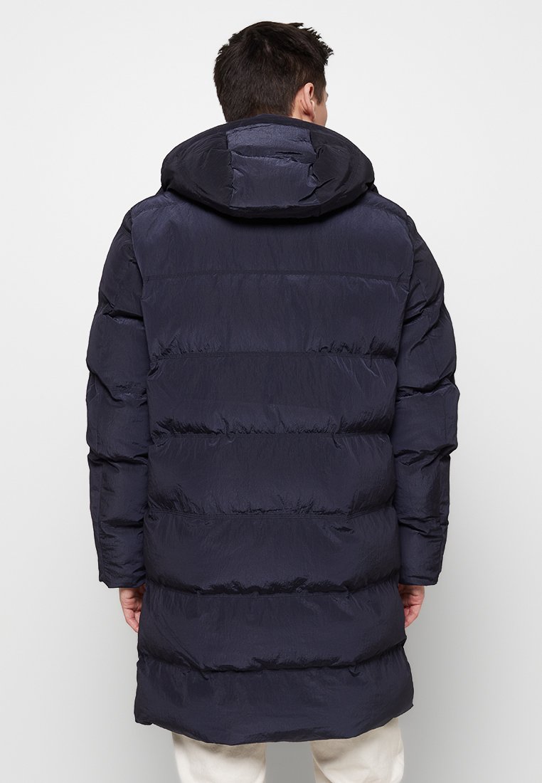 Marineblauwe pufferjas met een capuchon, voorzien van een gestikt ontwerp, lange mouwen en ribgebreide manchetten, gemaakt van een glad, lichtgewicht materiaal.
