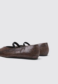 Chaussures plates à imprimé serpent marron avec des sangles élastiques noires, orteils arrondis et surface texturée. Design bas et semelle flexible.