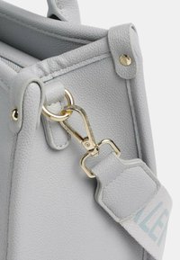 Borsa a mano in pelle grigia lavorata con accessori in oro, attacco a gancio e una tracolla con accenti blu chiaro. Inquadratura ravvicinata dei dettagli.