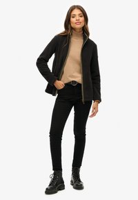 Czarna kurtka z złotym zamkiem, beżowy golf, czarne dżinsy i czarne sznurowane buty. Gładka tekstura, elegancki krój, dopasowana sylwetka.