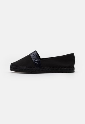 Sort slip-on espadrille med flettet sål og et blankt bånd øverst med præget tekst.
