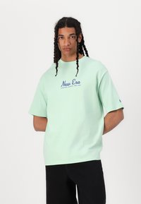 Lysegrøn T-shirt med korte ærmer og rund halsudskæring, med blå "New Era" tekst trykt på forsiden. Simpelt design, lavet af bomuldsstof.