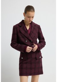Blazer à carreaux bordeaux avec un design croisé, accents de boutons en argent et jupe assortie. Tissu lisse avec une légère texture.