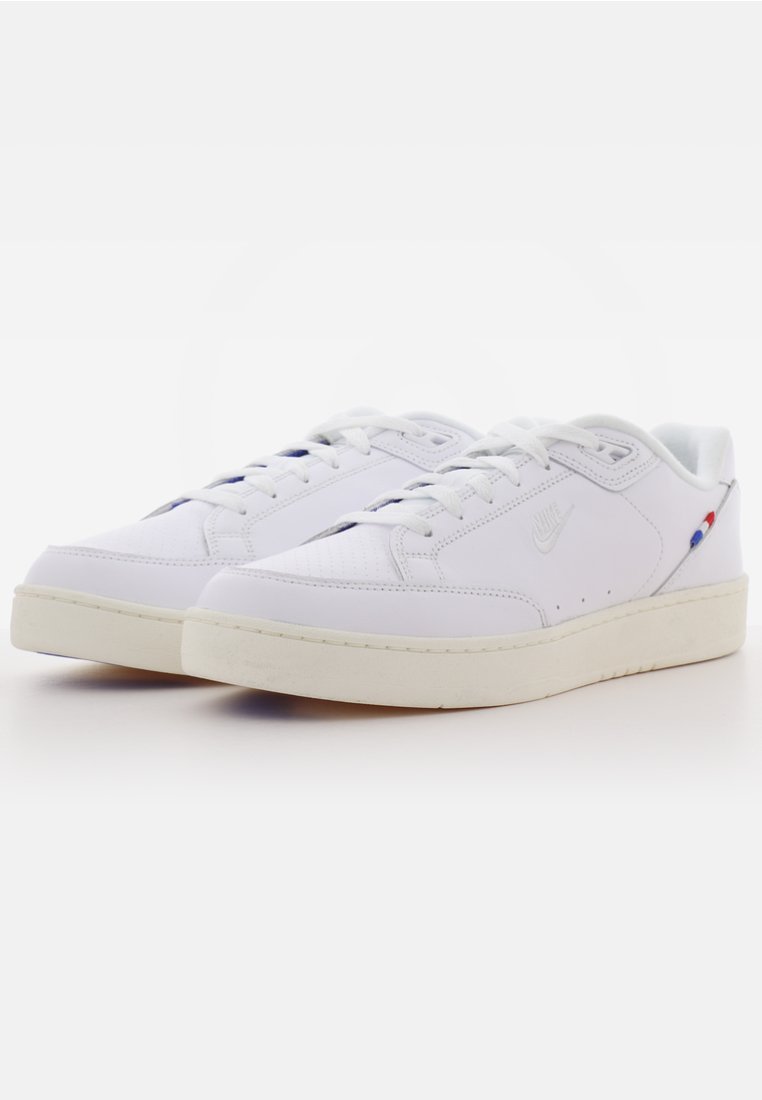 Ein Paar weiße Nike Low-Top-Sneaker mit durchlochter Zehenpartie, weißen Schnürsenkeln und roten sowie blauen Akzenten an der Ferse.