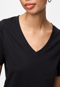 Musta V-kauluspaita pehmeästä puuvillasta, jossa on lyhyet hihat ja sileä pinta. Minimalistinen muotoilu ilman näkyviä kuvioita.