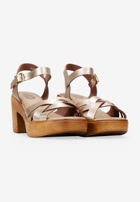 Gold metallic strappy sandals with a wooden heel, featuring crisscross straps and an ankle buckle. Flat sole and open toe design.
