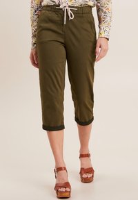 Pantaloni a vita alta di colore verde oliva realizzati in tessuto leggero, dotati di cintura elastica con cordino e orlo rifinito. Abbinati a sandali con piattaforma marroni.